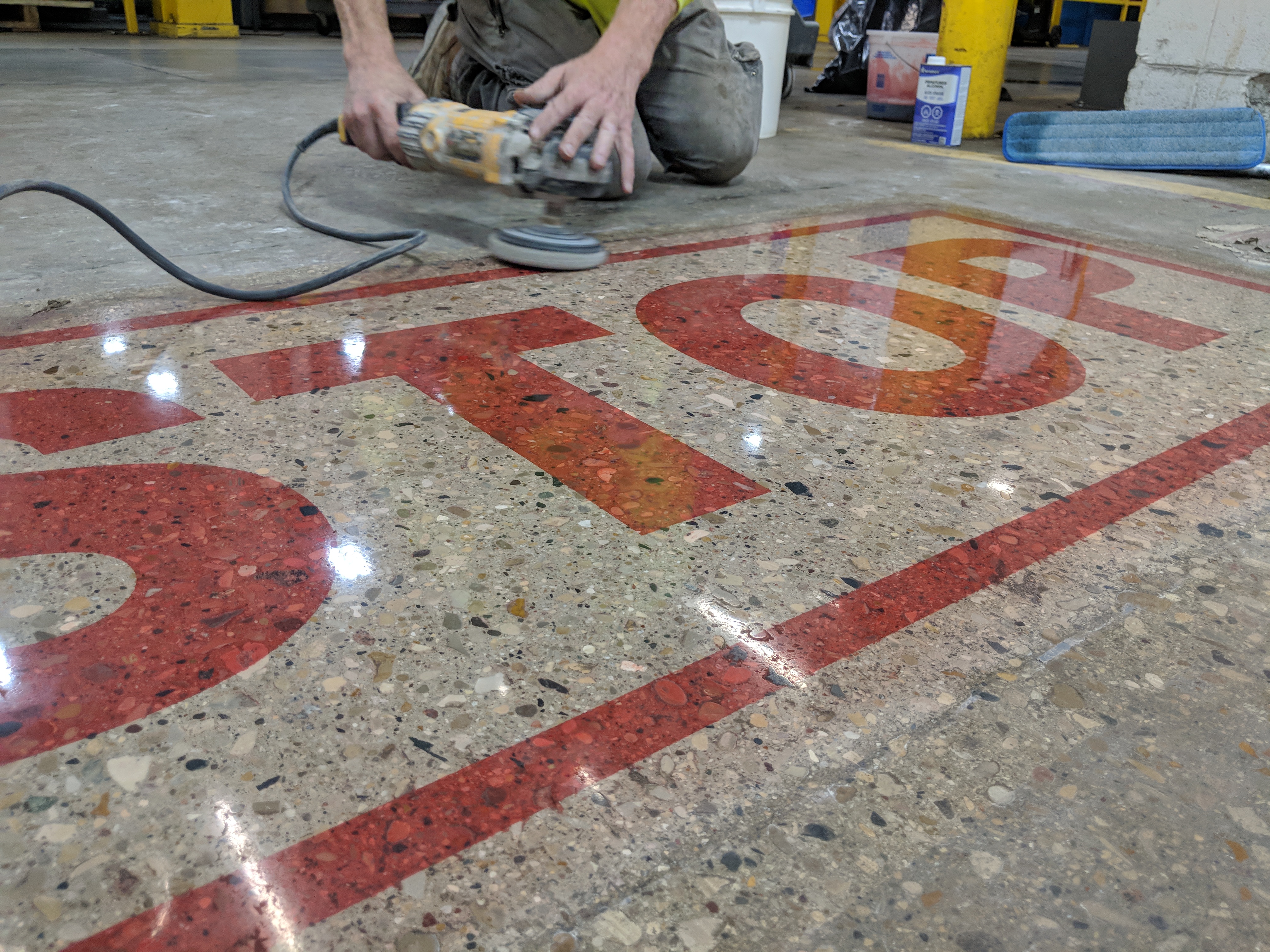 Quantum Crete installer hand-grinding a stained inlay detail in a polished concrete floor